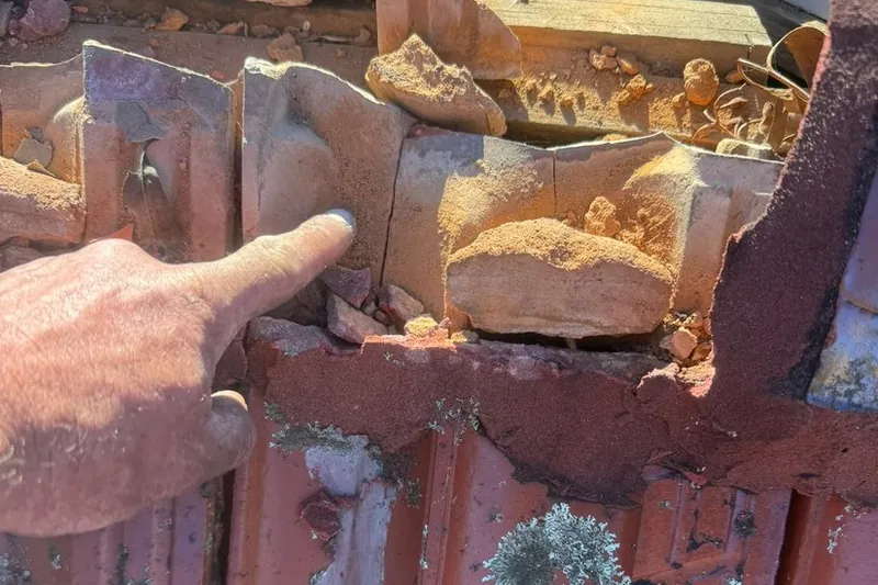 Roofer pointing to cracked cement bedding under the ridge capping