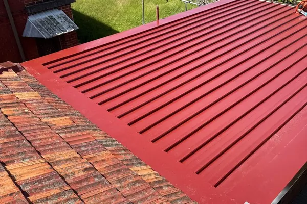 New red Colorbond roofing installed over part of a tiled roof