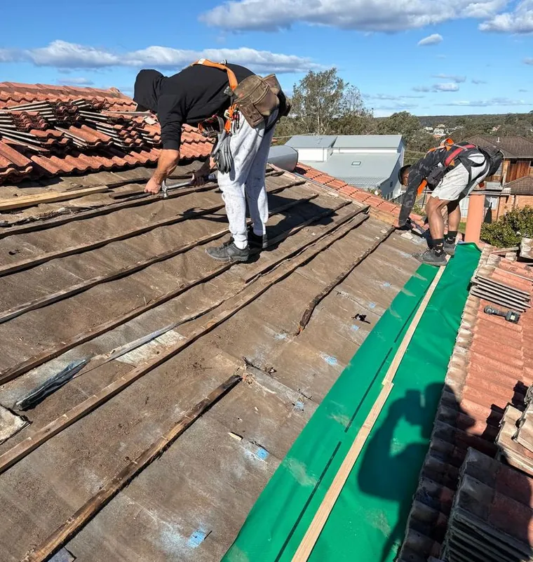 Two roofers fitting new sarking on a tiled Sydney roof